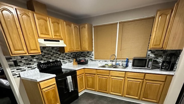 A modern kitchen with wooden cabinets, a black stove, a microwave, and a tiled backsplash.
