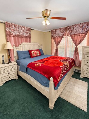 Une chambre à coucher comprenant un lit, des tables de chevet, une commode, un ventilateur de plafond et des rideaux.