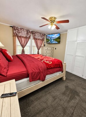 Une chambre à coucher comprenant un lit, un ventilateur de plafond, une télévision, une commode et une armoire.