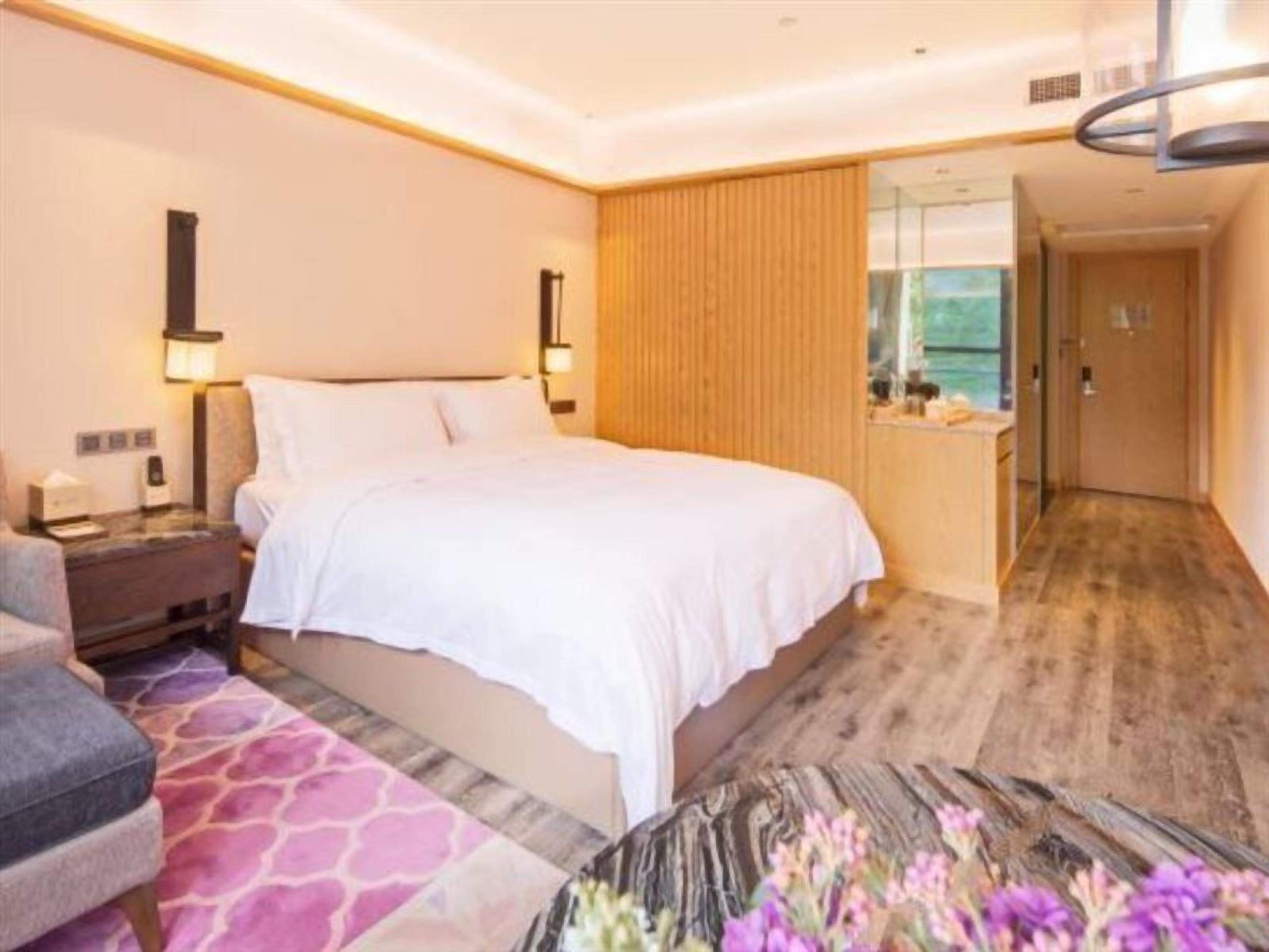 Habitación de hotel con cama, mesita de noche, lámpara y vista al exterior.