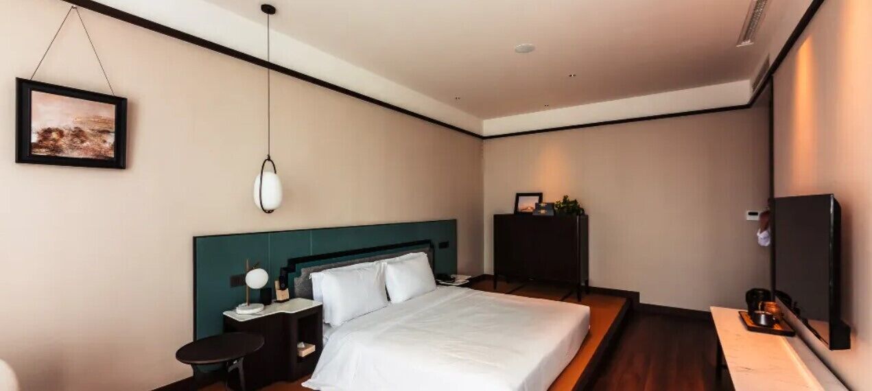 A modern hotel room with a large bed, bedside tables, a TV, and a framed picture on the wall.