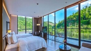 Un dormitorio moderno con una cama grande, un escritorio pequeño y un balcón con vistas a zonas verdes.