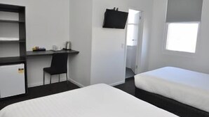 A room with a bed, a desk with a chair, a TV mounted on the wall, and a window. - Queens Head Hotel (Hobart)