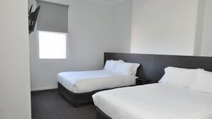 Hotellihuone, jossa on kaksi sänkyä, ikkuna ja tumma pääty.