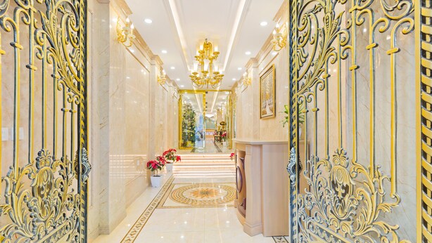 A luxurious hallway with ornate metal railings, a marble floor, and a chandelier.