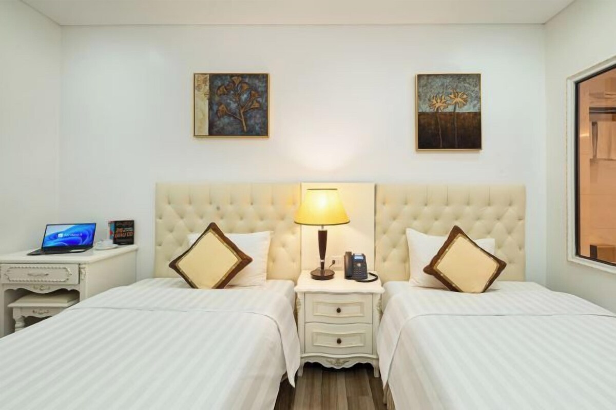 Habitación de hotel con dos camas, un escritorio con una computadora portátil, una lámpara y dos cuadros en la pared.