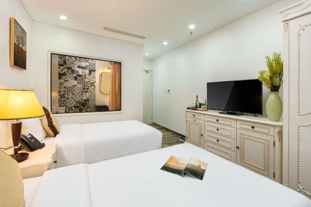 Habitación de hotel con dos camas, televisor, minibar y un espejo decorativo.
