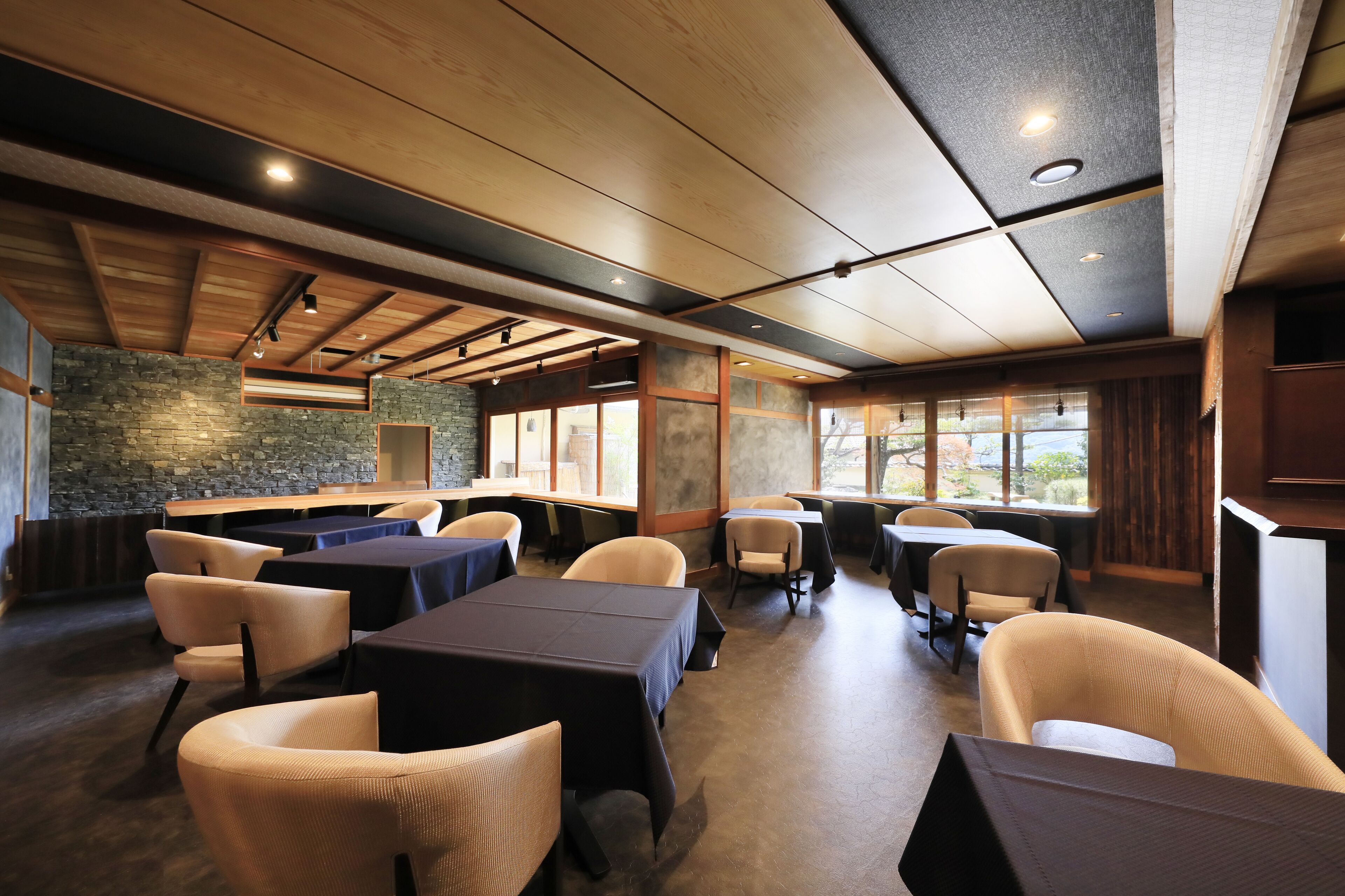 A restaurant with a stone wall, wooden ceiling, and tables with dark tablecloths.