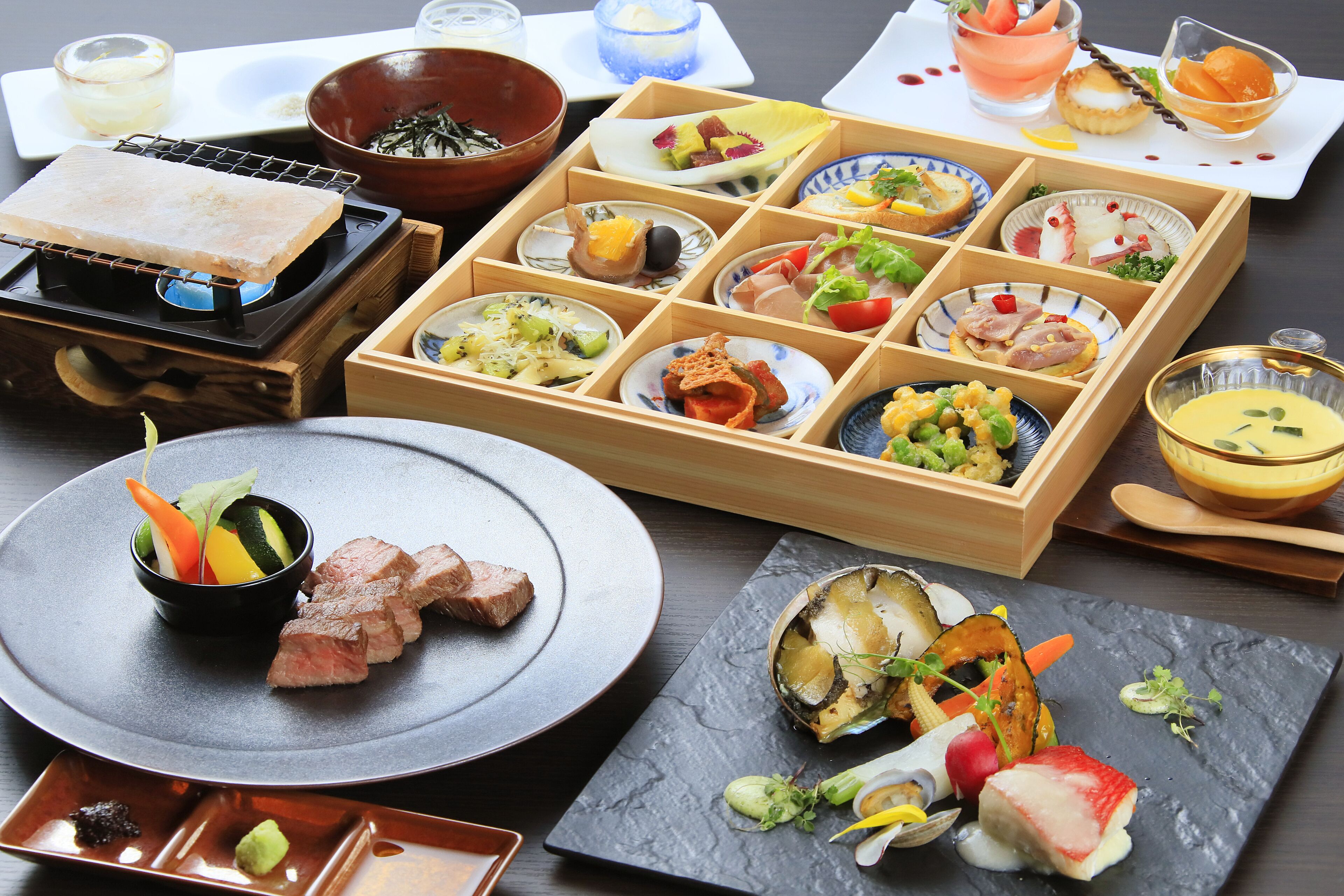 A variety of dishes and food items arranged on a table, including a hot plate, bowls, and plates with different types of food.