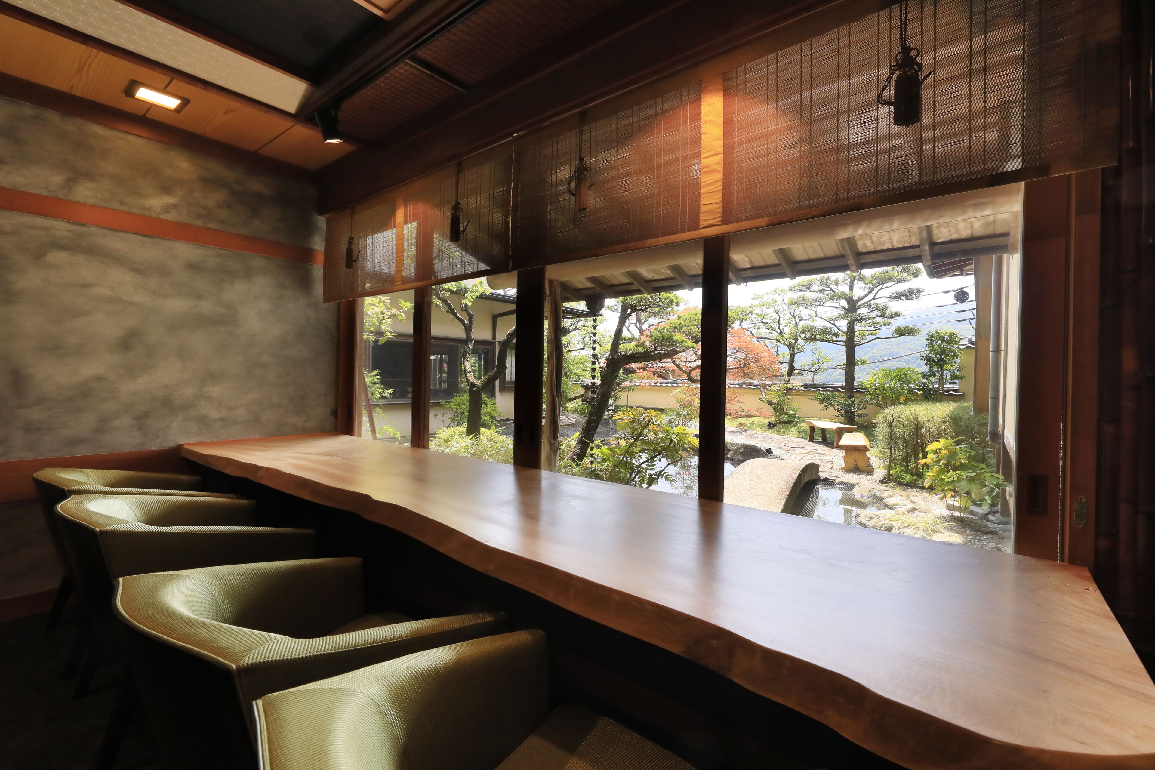 Una larga mesa de madera con sillas, vista a un jardín a través de una ventana y un diseño de techo tradicional.