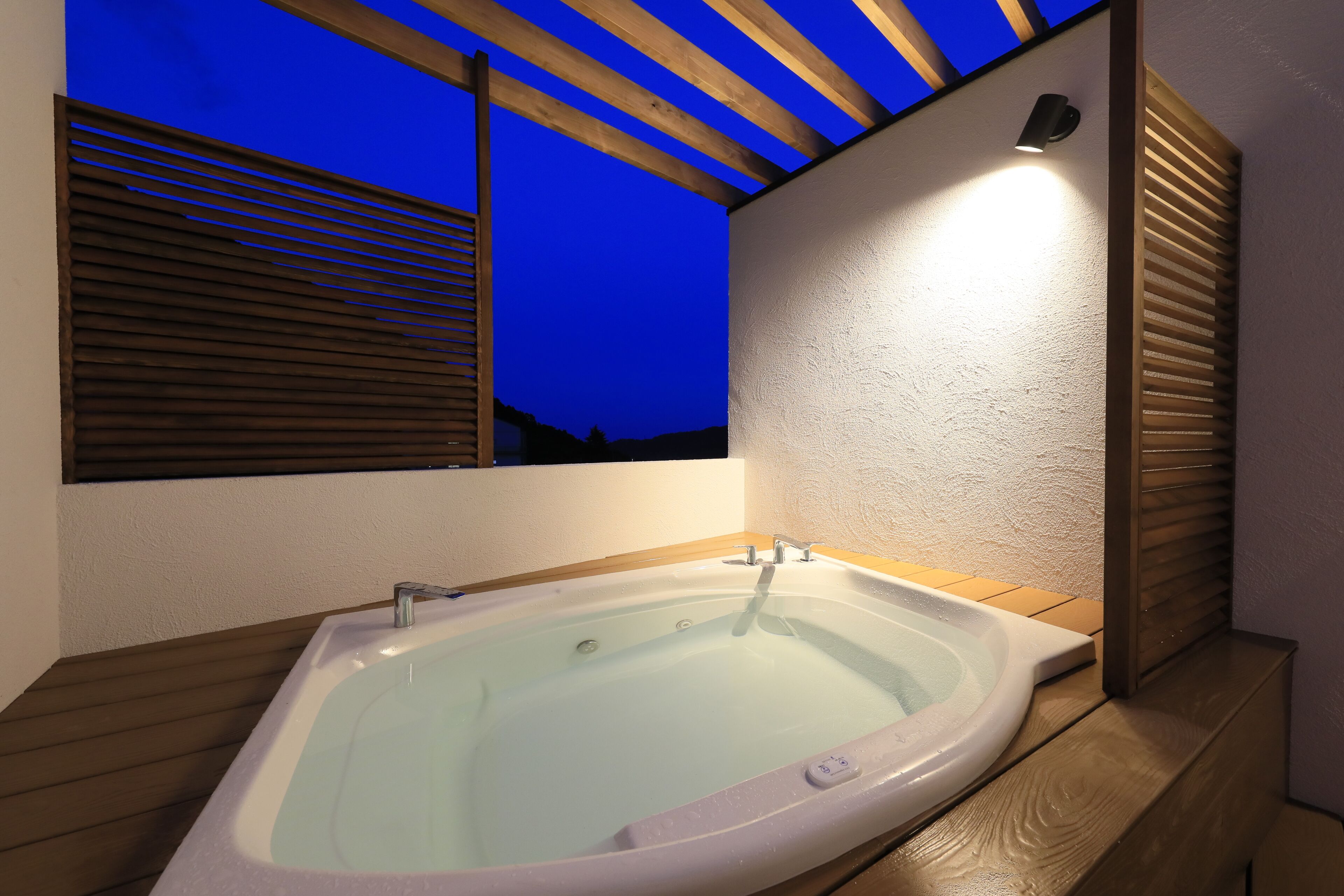 A modern bathroom with a freestanding bathtub, wooden slats, and a view of the night sky.