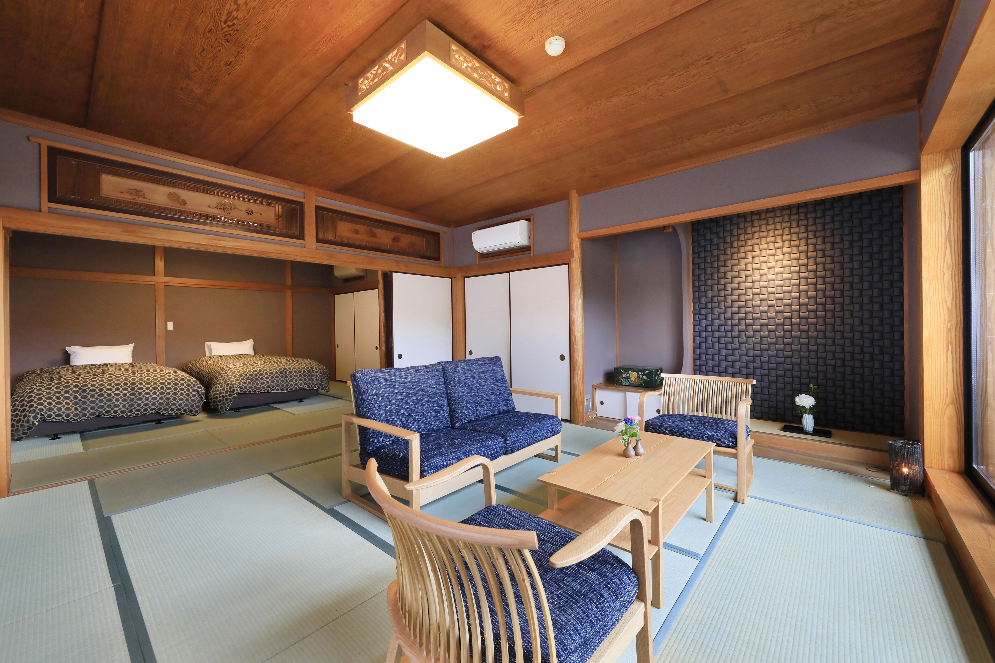 Una habitació japonesa tradicional amb sòls de tatami, un sofà blau, una taula de fusta i una cadira amb tatami.