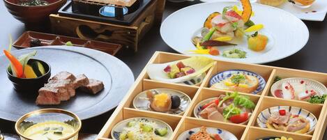 A variety of dishes and food items arranged on a table, including plates, bowls, and a wooden box with compartments.