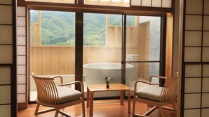 A room with a wooden floor, two rocking chairs, a small table with a vase, and a large window offering a view of a forested area. - Yugarawa Fuga (Yugawara)