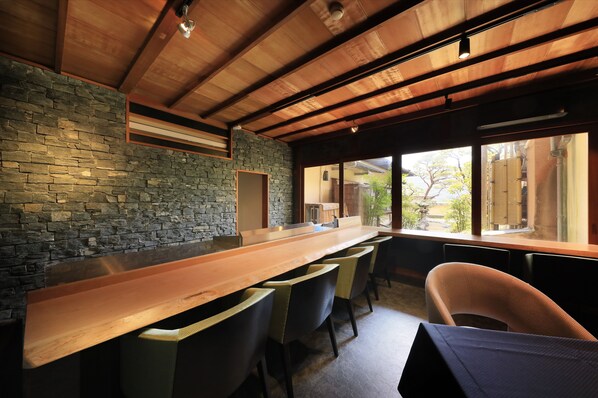 Un espace bar moderne avec un mur en pierre, des poutres en bois au plafond et un long comptoir agrémenté de chaises.