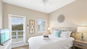 A hotel room with a bed, a nightstand, a TV, and a balcony with blinds. - Sandcastles by the Sea 402 - 30A, Community Pool, Steps to the Beach! (Blue Mountain Beach)