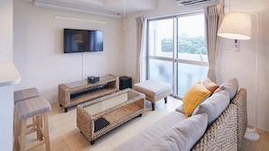 Una sala moderna con una televisión de pantalla plana, muebles de mimbre, un sofá con cojines y un ventanal con cortinas.