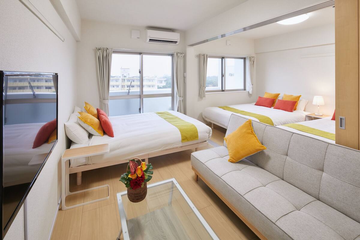 A hotel room with two beds, a sofa, a TV, and a window with curtains.