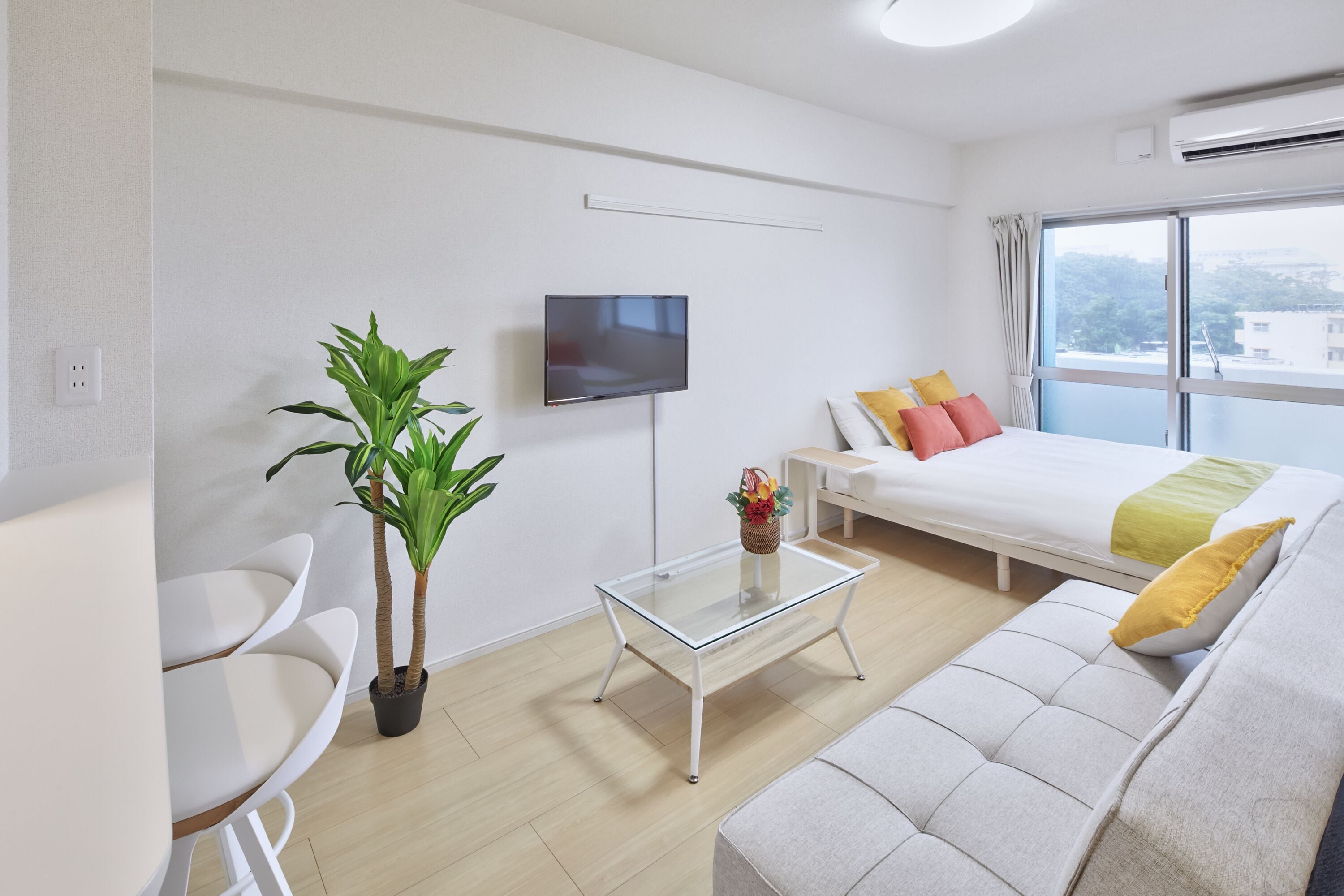 Ett modernt hotellrum med en säng, soffa, TV och ett litet bord med en växt.