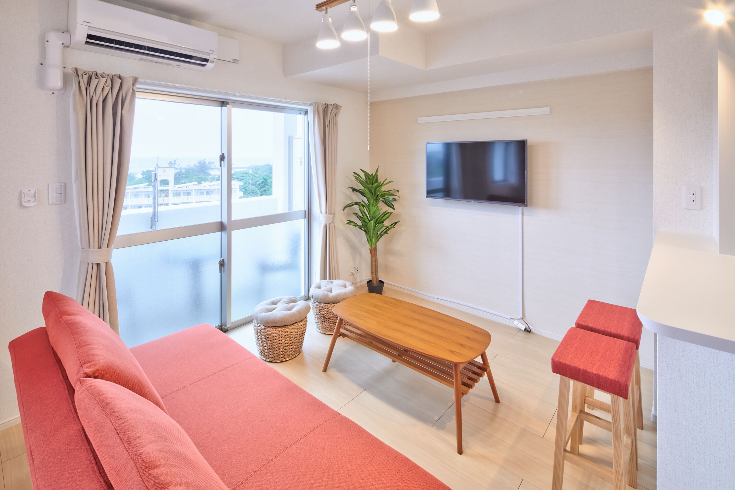 Una sala de estar moderna con un sofá, una mesa de madera, dos taburetes altos, un televisor y un ventanal con cortinas.