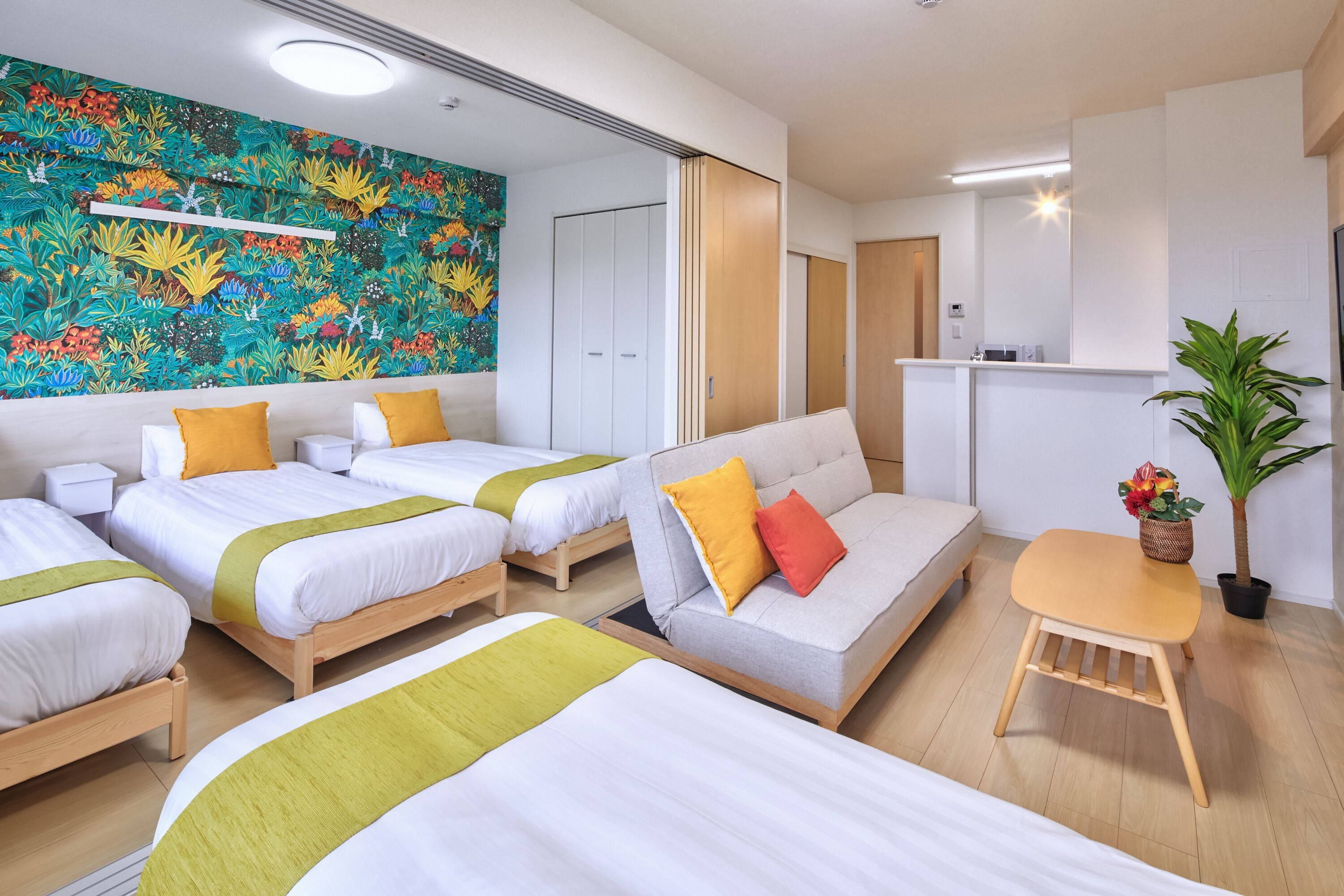 A hotel room with two beds, a sofa, a small table, and a colorful mural on the wall.