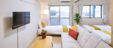 A hotel room with a flat-screen TV, a sofa, a bed, a small table with a vase, and a window with curtains.