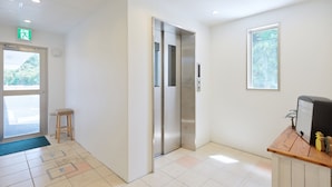 Un vestíbulo moderno y cuidado, con mostrador de recepción, ascensor y puerta de acceso al exterior.