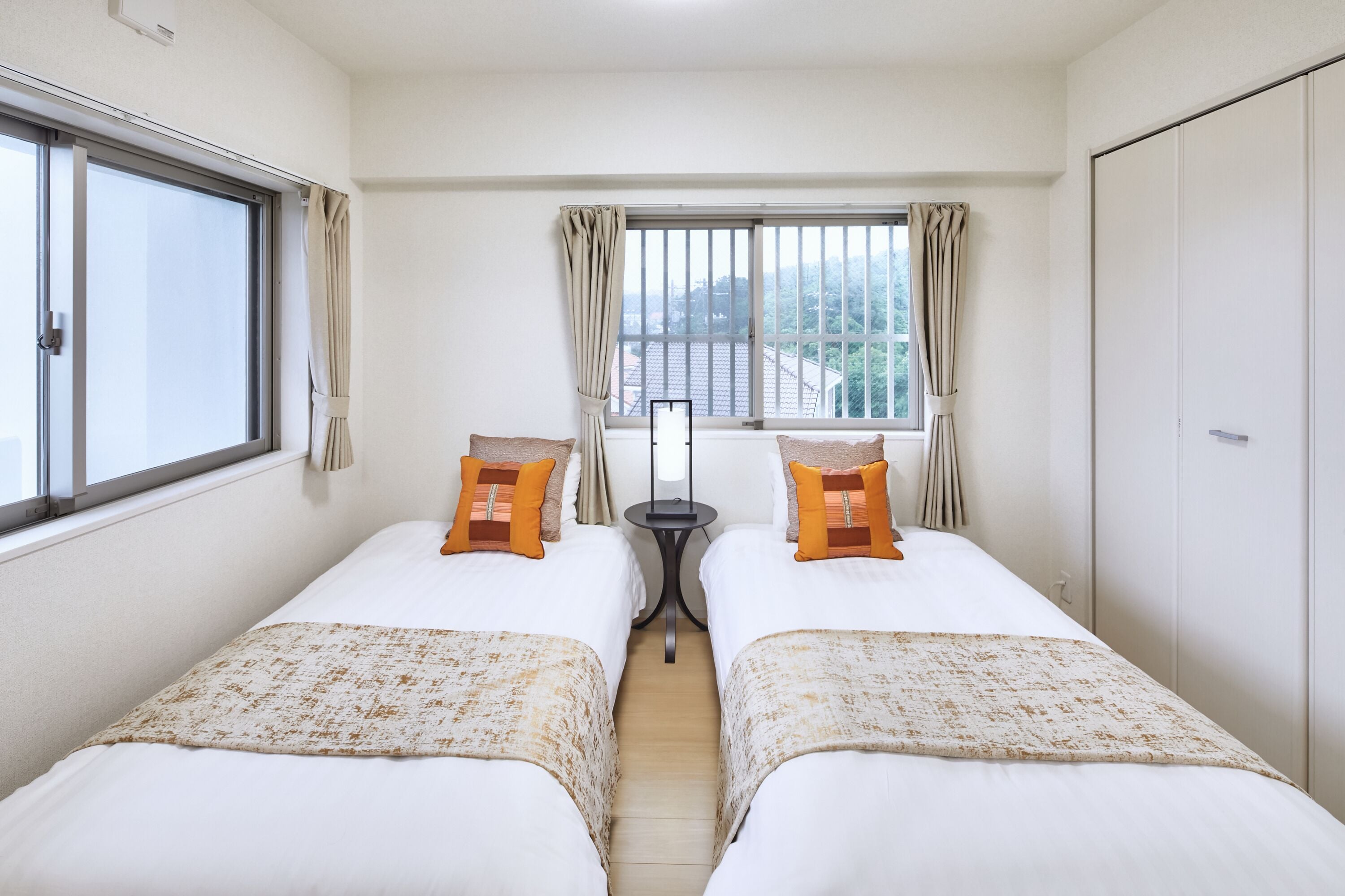 A hotel room with two beds, a window with curtains, a small table, and a wardrobe.