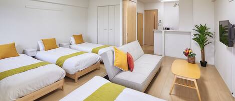 A hotel room with three beds, a sofa, a small table, and a potted plant.