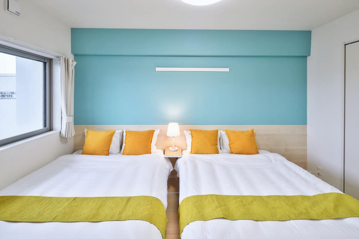 A hotel room with two beds, a window, and a nightstand with a lamp.