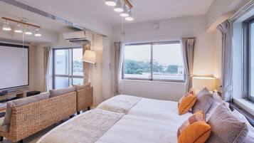 A hotel room with a large bed, a sofa, a TV, and a window with a city view.