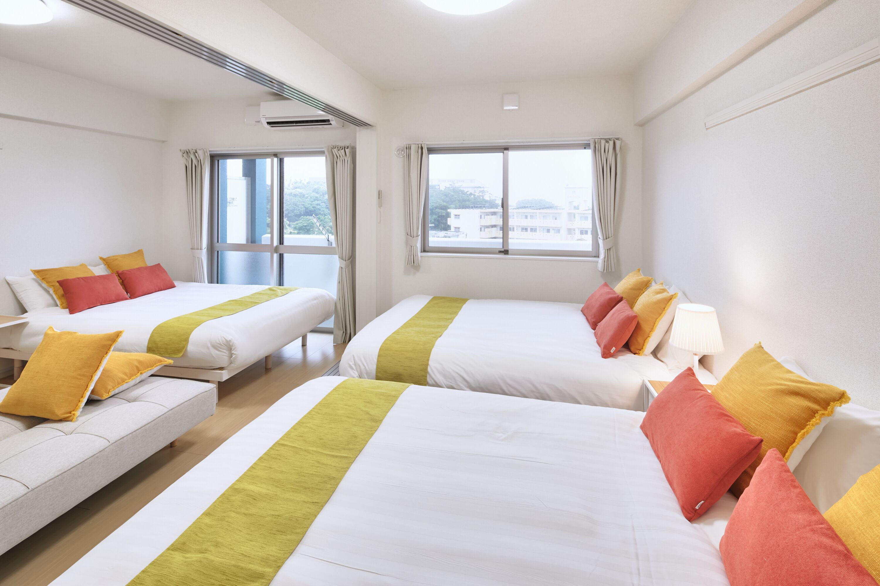 Une chambre d’hôtel avec deux lits, chacun agrémenté de draps blancs et de touches de couleur jaune, un canapé avec des coussins jaunes et une fenêtre avec des rideaux.