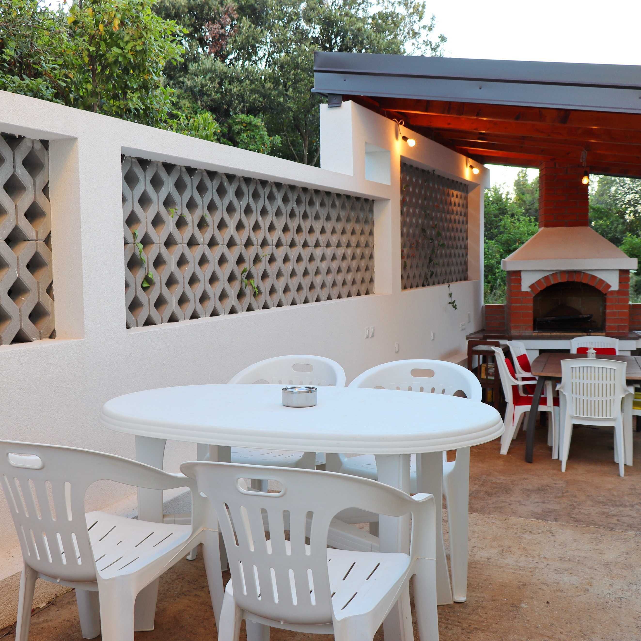 Un patio al aire libre con un horno de ladrillo, sillas de plástico blanco y una mesa.