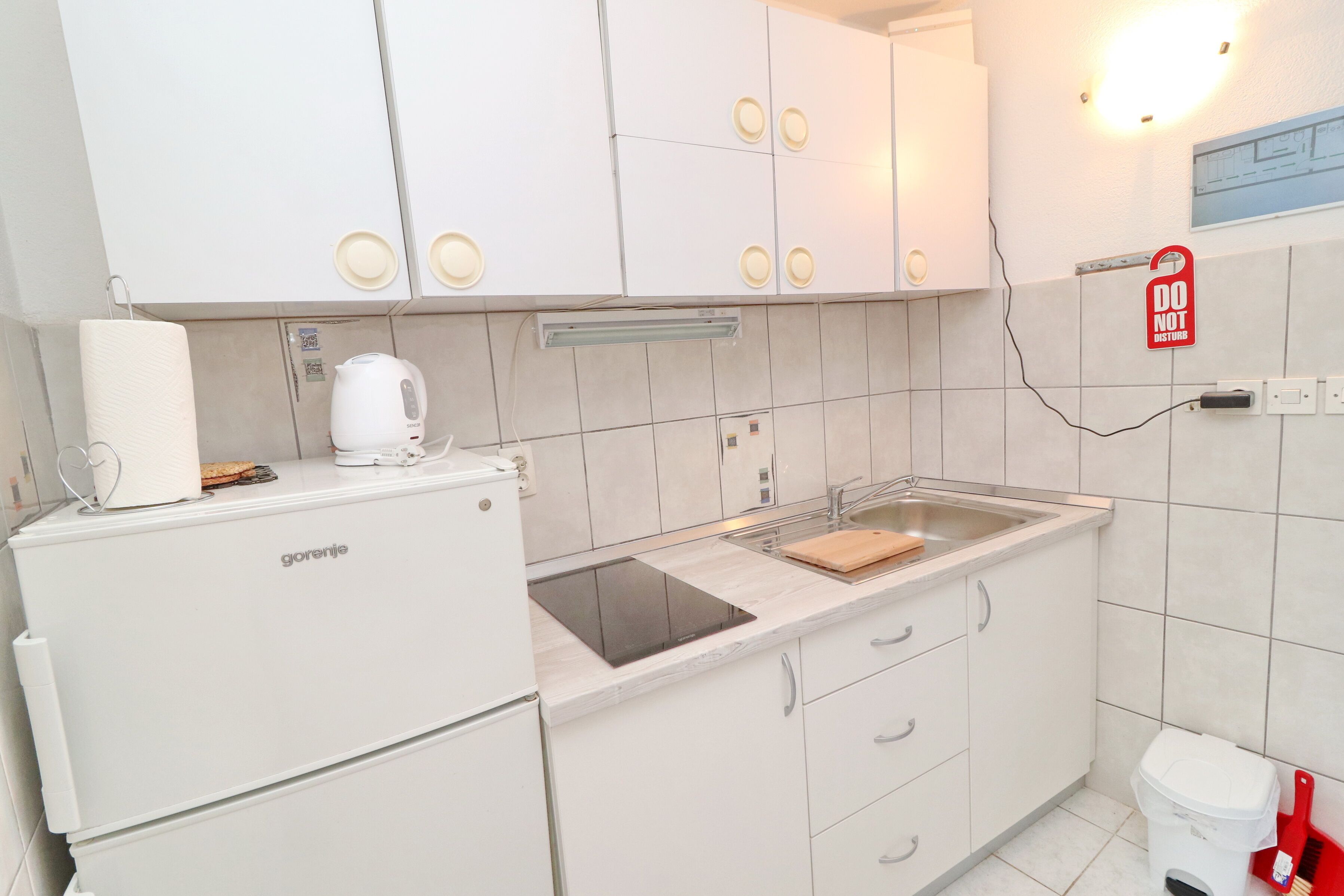 Een kleine keuken met een koelkast, een koffiezetapparaat, een spoelbak en een 'NIET STOREN'-bordje.