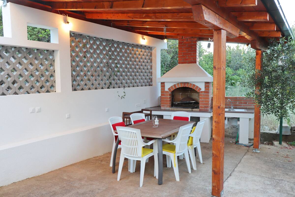 An outdoor patio with a brick oven, white chairs, and a table.