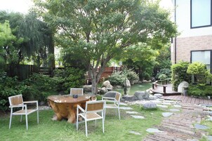 Un jardín con una mesa y sillas de madera, un pequeño estanque y un edificio de ladrillo al fondo.