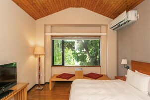 Un dormitorio con cama, televisor, ventana con vistas a árboles y aire acondicionado.