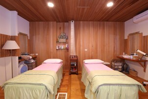 Una habitación con dos camas, paredes de madera, un ventilador de techo, un estante con artículos de aseo y un espejo.