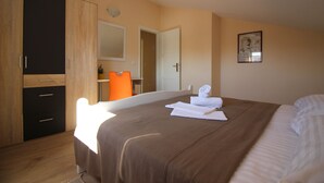 A bedroom with a large bed, a wardrobe, a mirror, and a door leading to another room.
