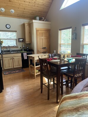 Una cocina con armarios de madera, una mesa de comedor con sillas y un ventanal con persianas.