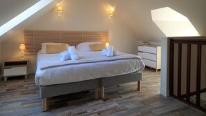 Une chambre avec un plafond en pente, un grand lit avec du linge de lit blanc, deux lampes de chevet et une tête de lit en bois.