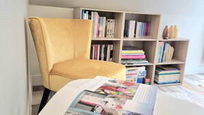 Une pièce avec une chaise jaune, une bibliothèque remplie de livres et une table avec des magazines.