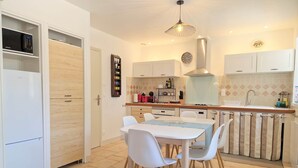 Une cuisine moderne avec des meubles blancs, une table à manger avec des chaises et un luminaire suspendu.