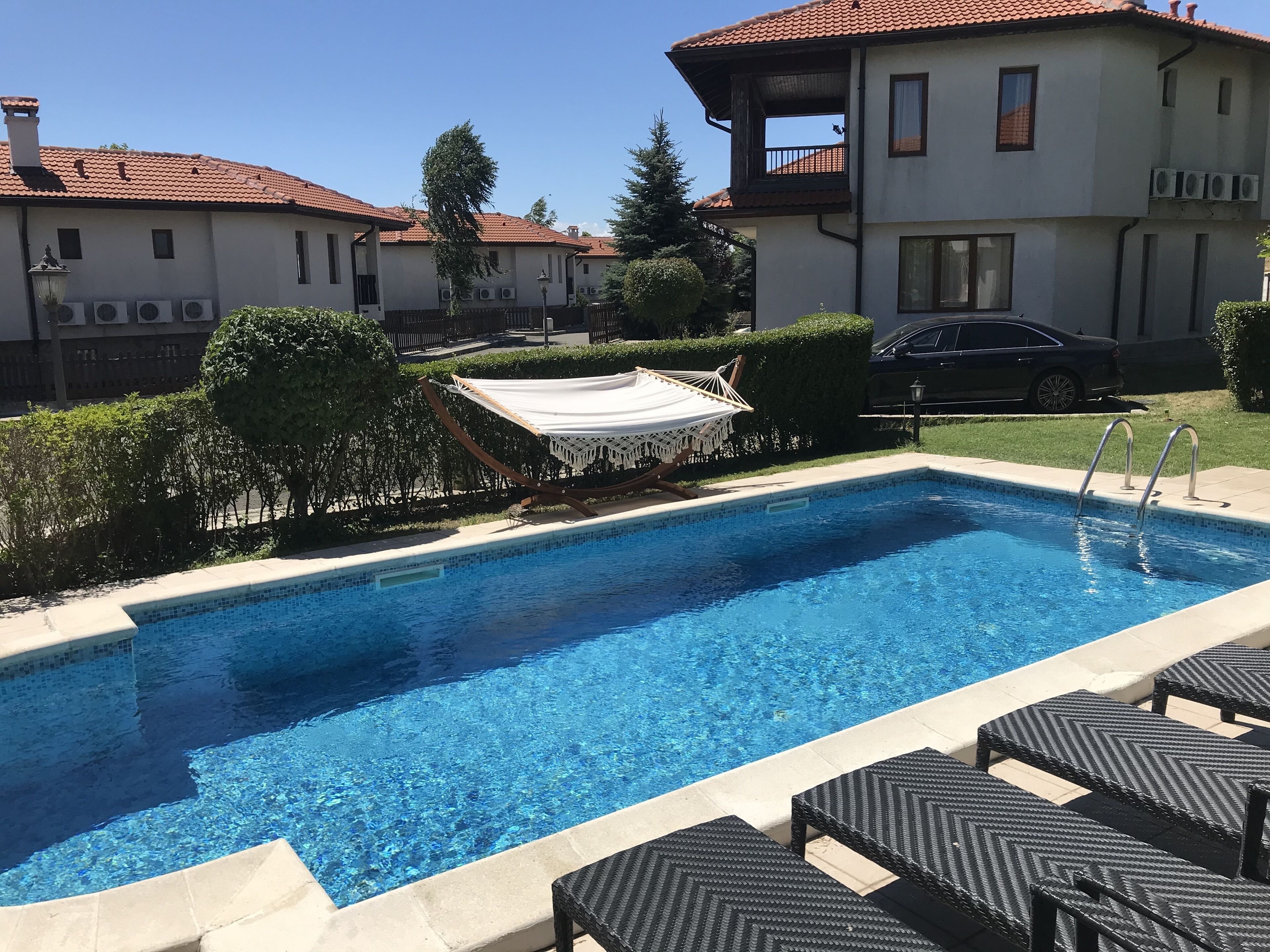 A swimming pool with lounge chairs, a hammock, and a car parked nearby.