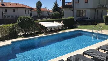 A swimming pool with lounge chairs, a hammock, and a car parked nearby.