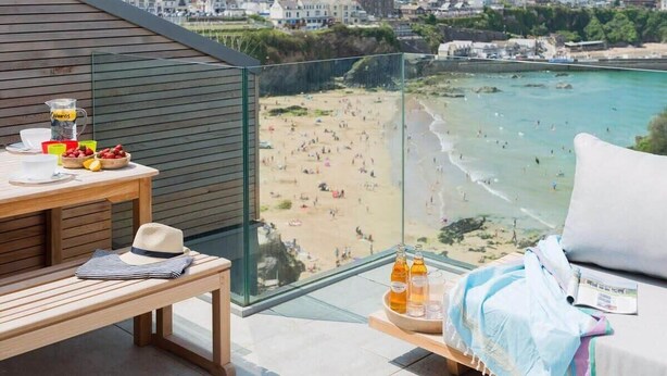 A balcony with a view of a beach, a table with drinks and snacks, and a bench. - Beachfront Townhouse, Lovely Sea Views, Newquay (Newquay)