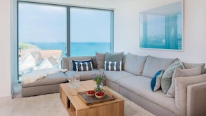 A modern living room with a large window, a sofa set, a coffee table, and a view of the sea. - Beachfront Townhouse, Lovely Sea Views, Newquay (Newquay)