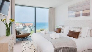 A modern bedroom with a large bed, a TV mounted on the wall, and a view of the sea. - Beachfront Townhouse, Lovely Sea Views, Newquay (Newquay)