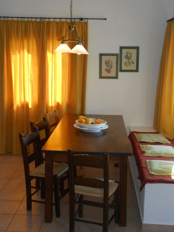 Un coin repas avec une table en bois, des chaises, un saladier de fruits et deux tableaux encadrés accrochés au mur.