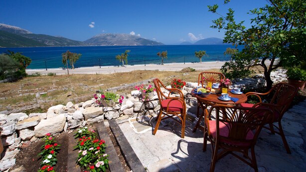 Tavolo apparecchiato all'aperto con sedie, un muro in pietra e vista mare e montagne.